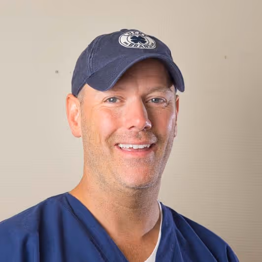 Smiling man, Sean, wearing a navy blue cap and blue scrub top against a plain background.