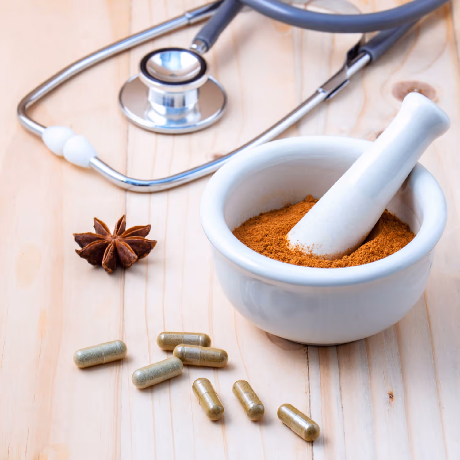 Mortar with ground spice and pestle, star anise, herbal capsules, and stethoscope on wood surface.