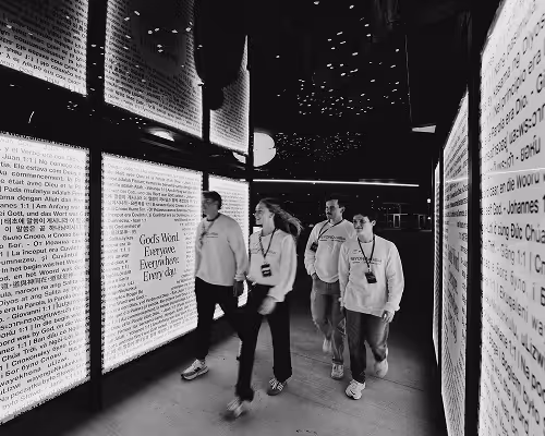 Four people walking through a dim corridor with large illuminated text panels on each side.