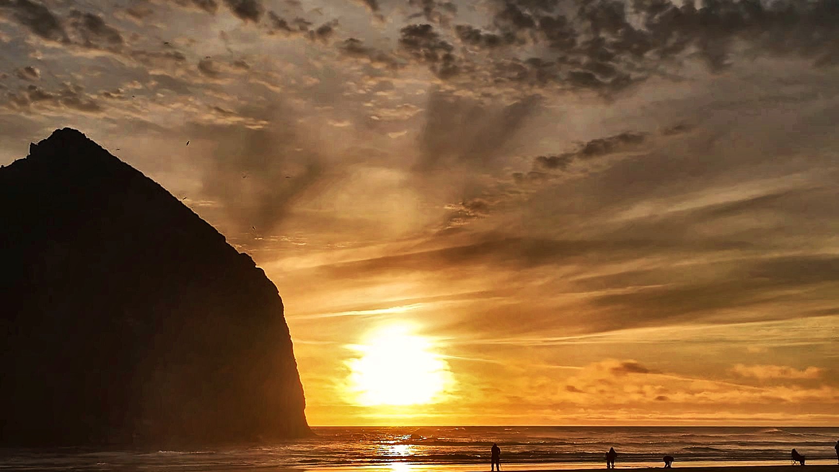 Sun setting beside Haystack Rock with the family on the shoreline, Cannon Beach