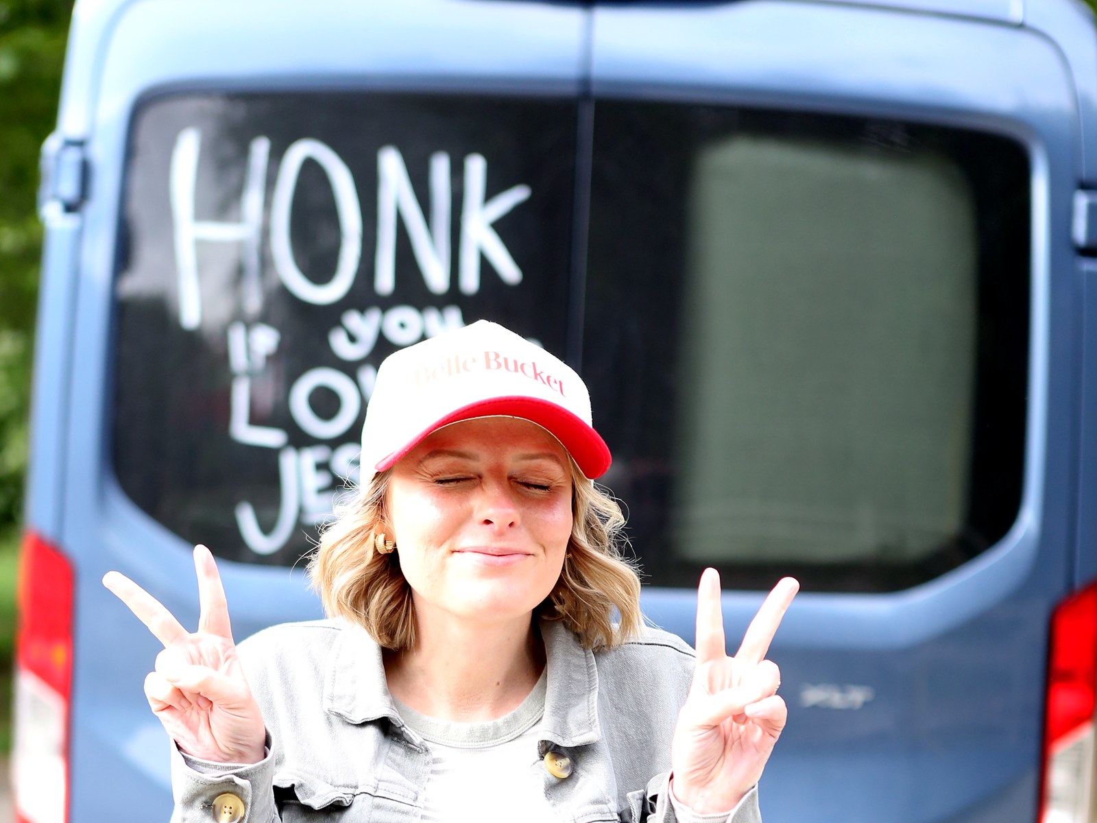 Amy in a Belle Bucket cap flashing two peace signs in front of the family van