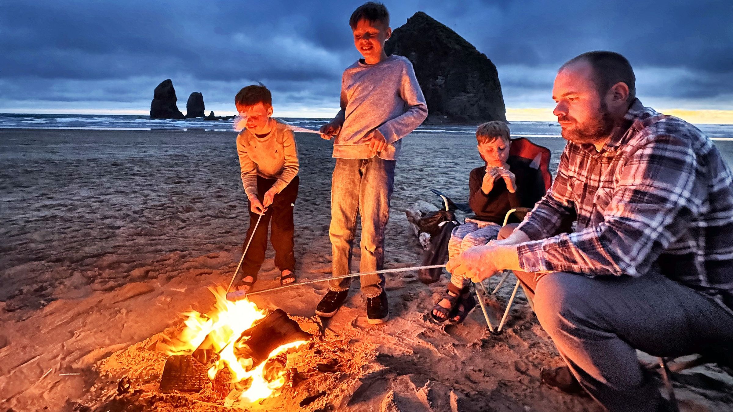 Chris and the boys around a campfire on the beach at Cannon Beach, Haystack Rock behind them