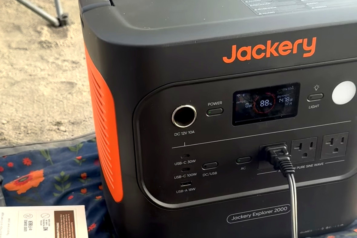 Our Jackery Explorer 2000 on a picnic blanket in the sand, plugged in and running, with the oatmeal boxes next to it