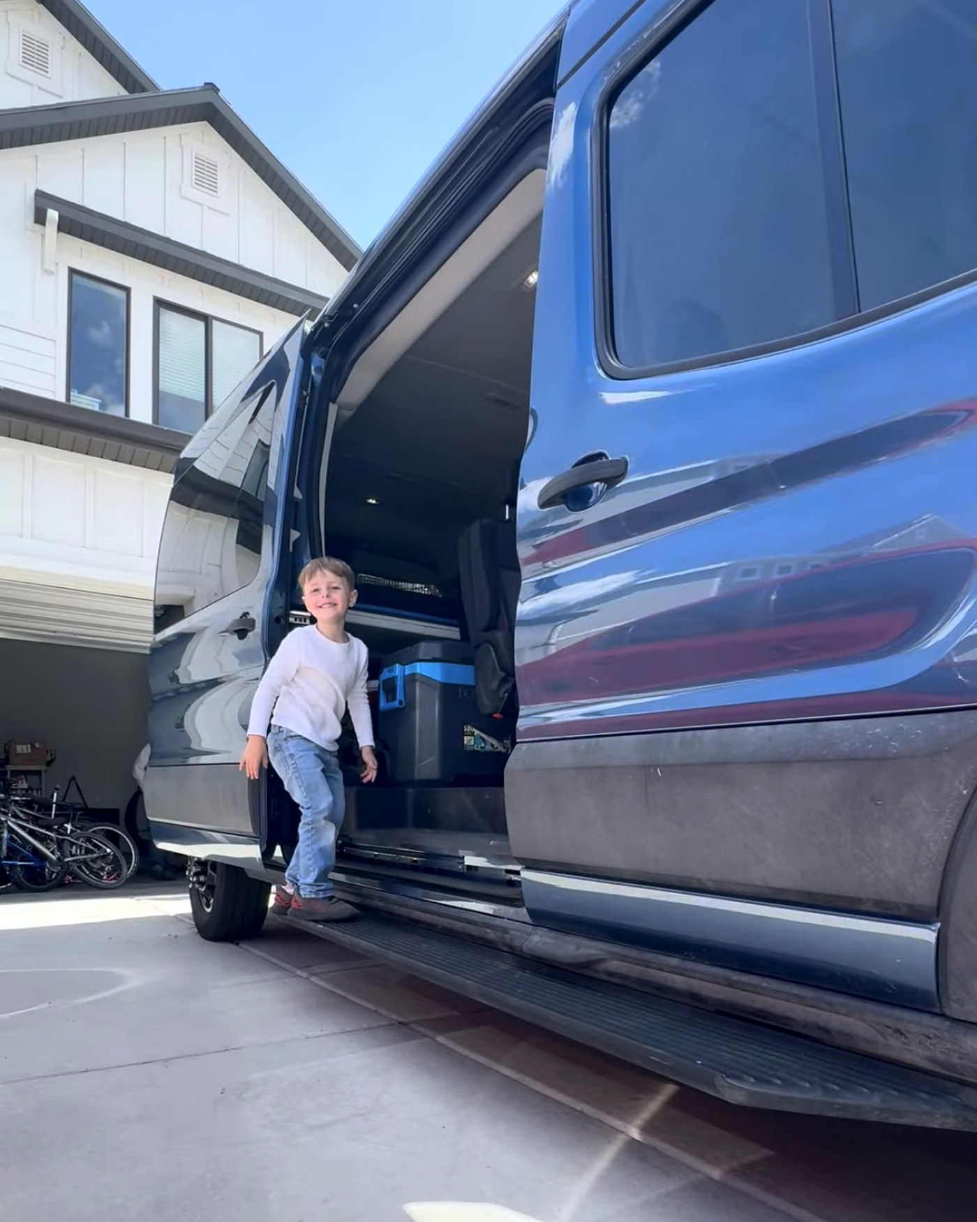 One of the boys hopping out of the open side door of the big blue van in our driveway