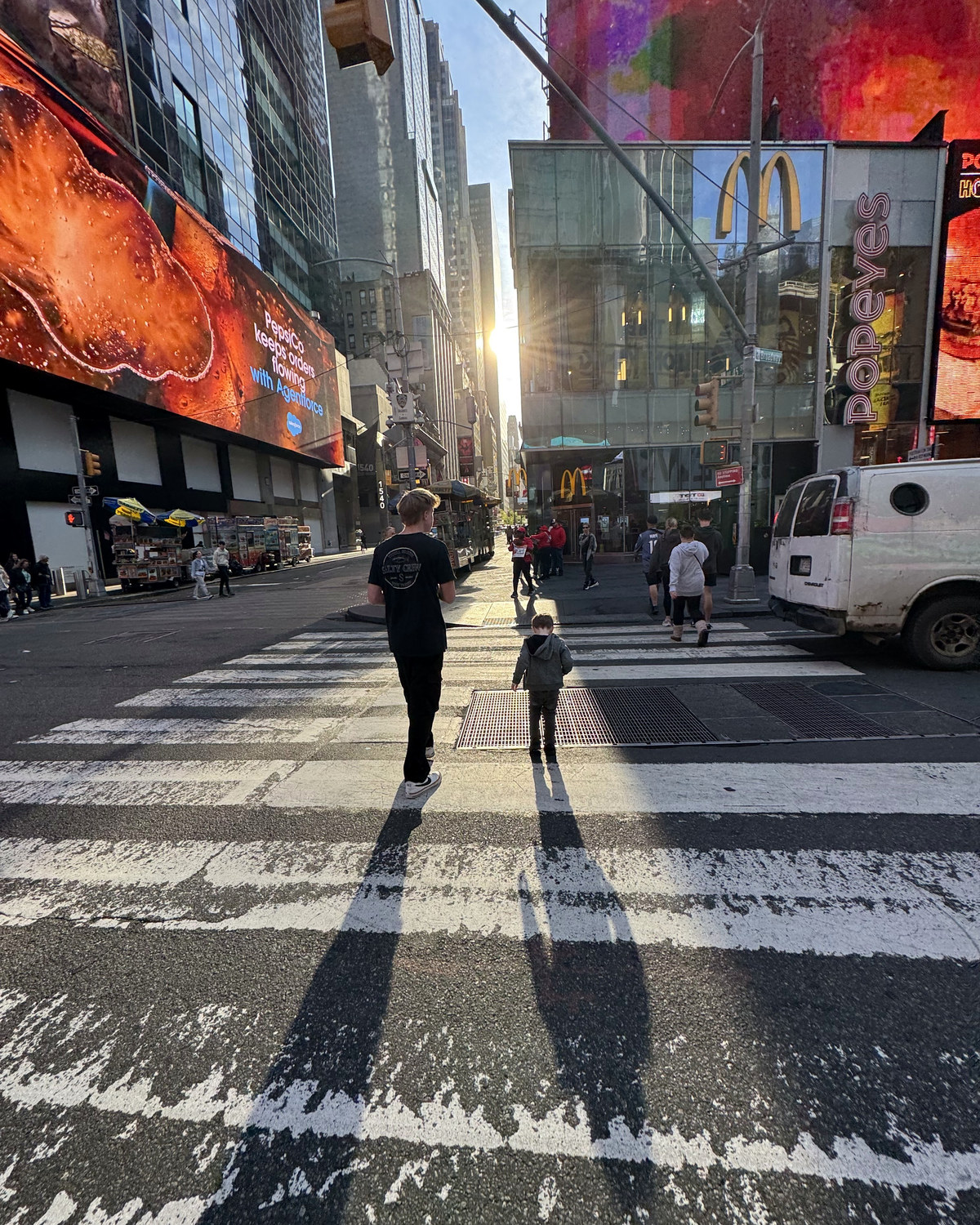 Two of the boys crossing the street in Times Square with the sun coming down the block