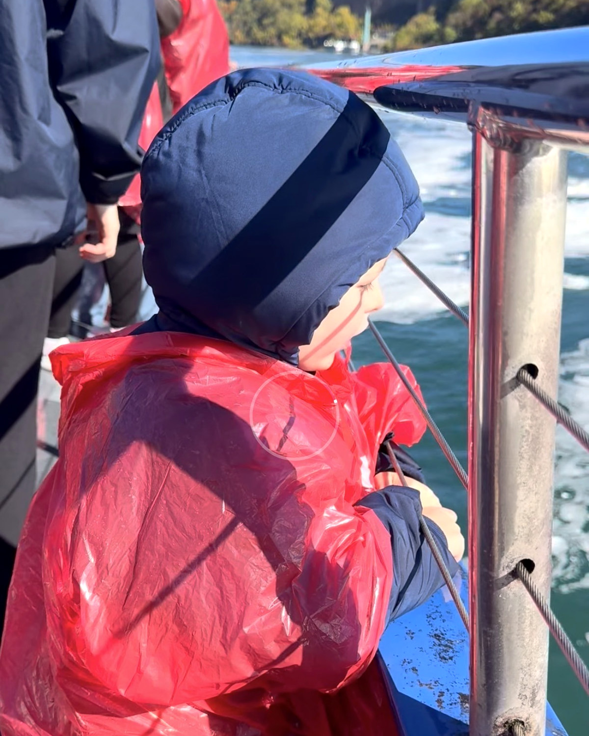 One of the boys in a red poncho at the boat rail on the Niagara River, the bridge behind him