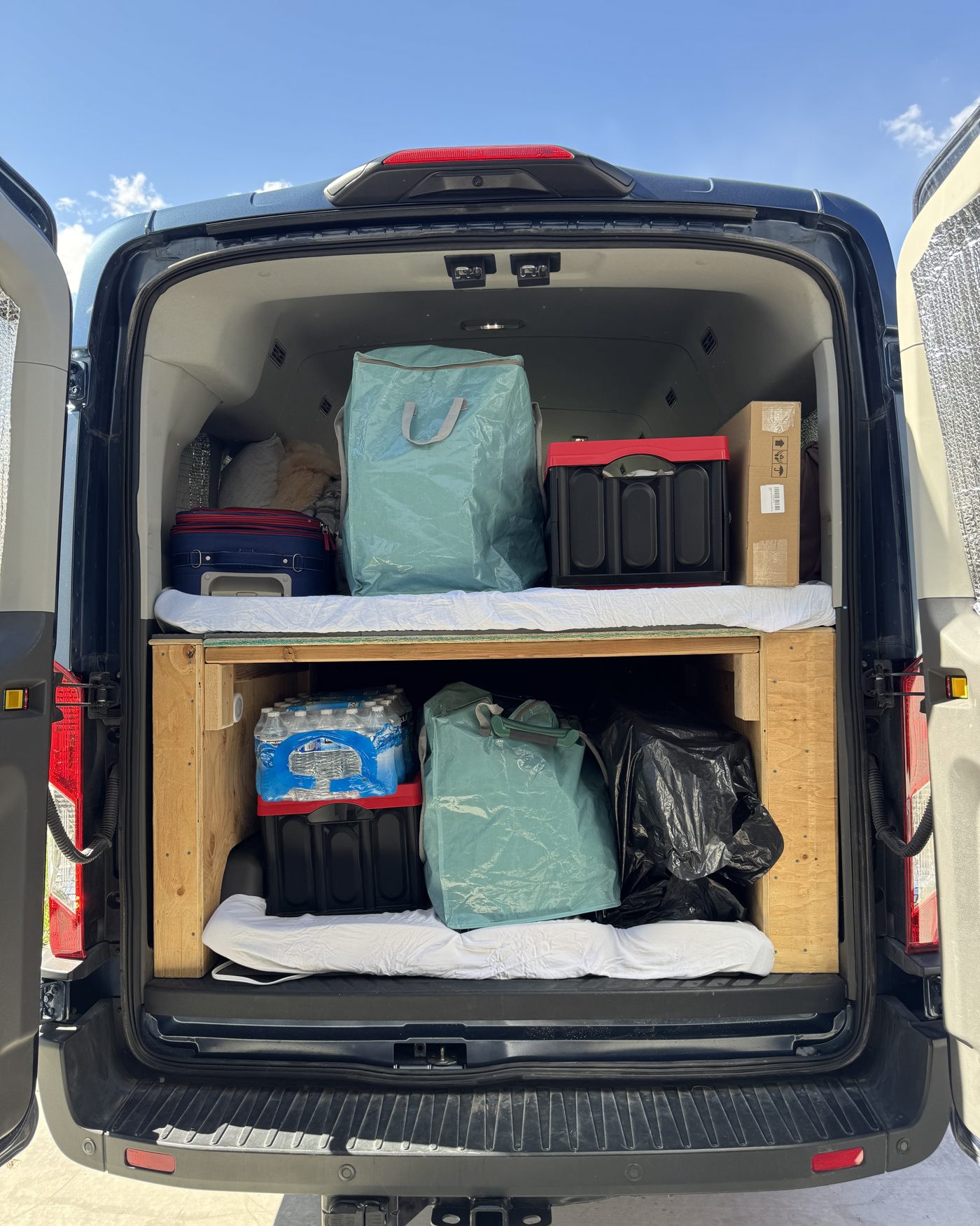 The back of our Ford Transit packed for a road trip, bins and a cooler on a wooden platform