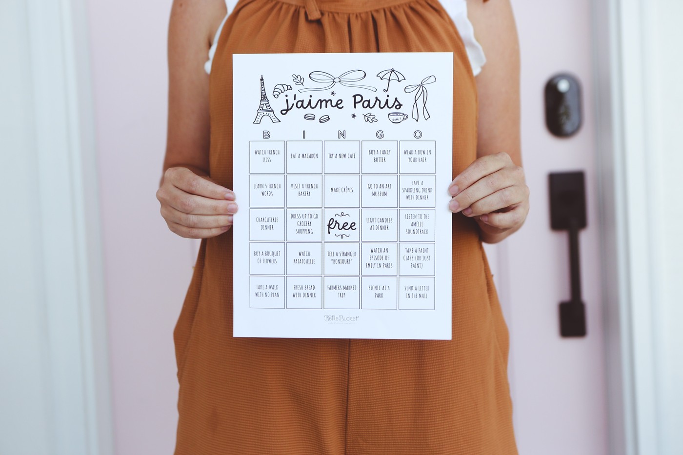 j'aime Paris bingo card printable, held up in front of a pink door