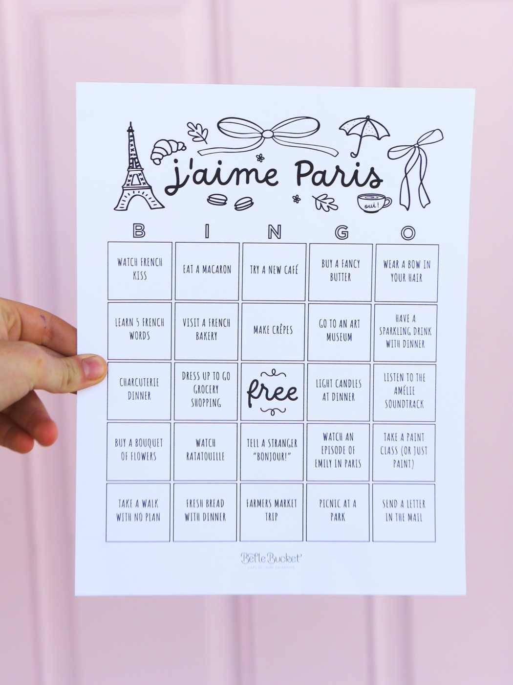 j'aime Paris bingo card printable, held up in front of a pink door