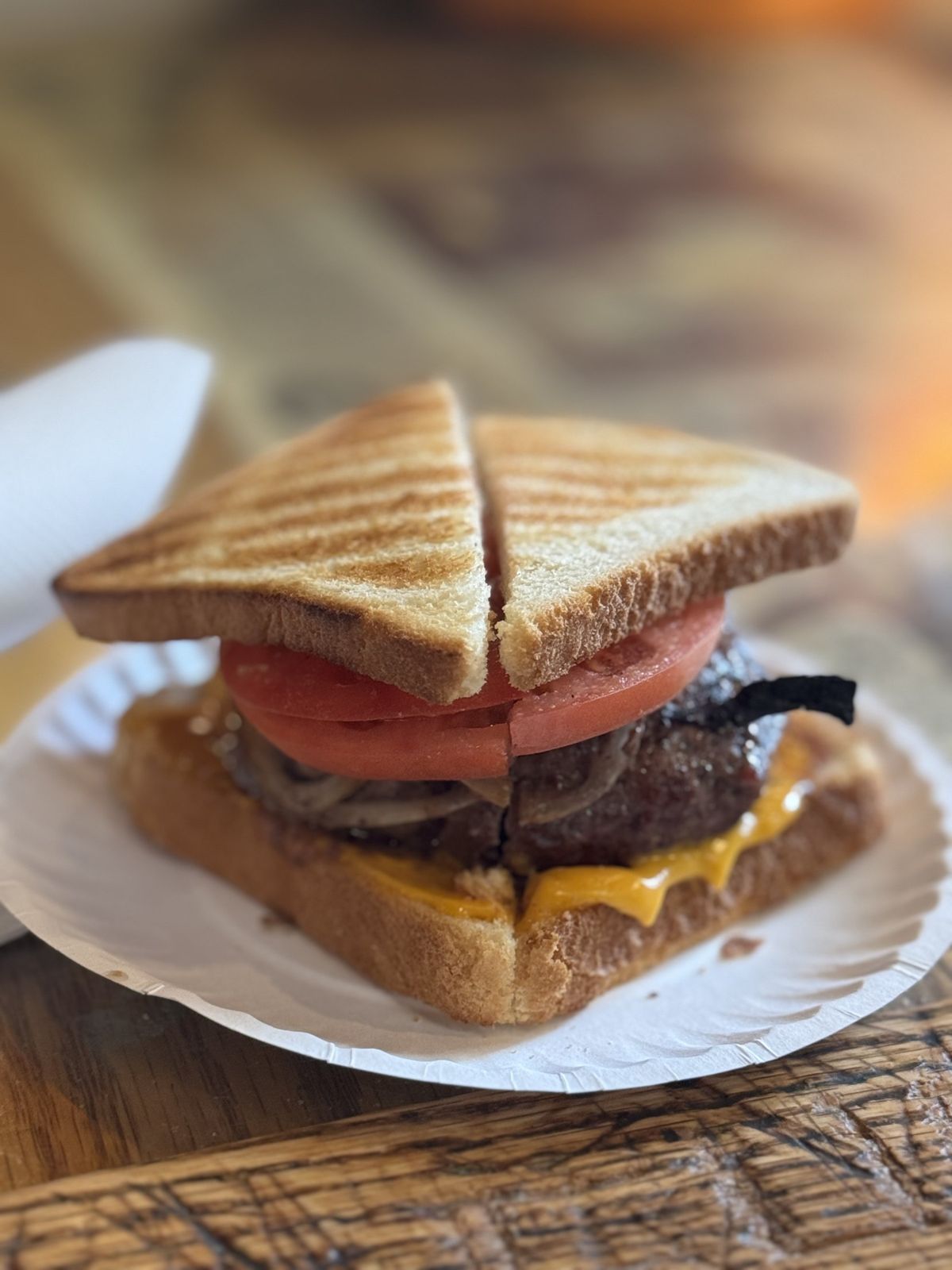 A Louis' Lunch hamburger on toast with tomato and cheese on a paper plate