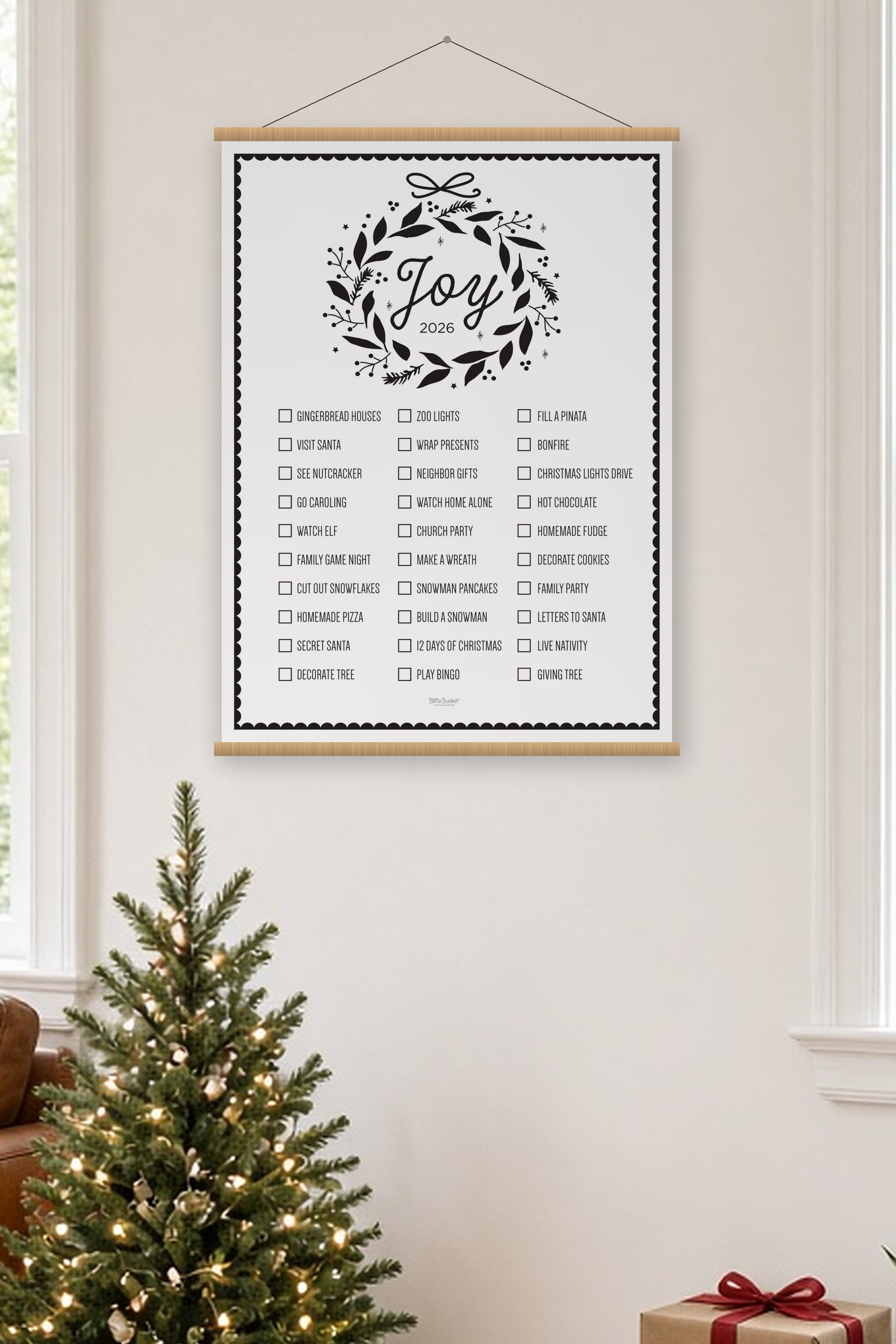 Joy Christmas bucket list poster, 36 by 48 inches, hanging on oak rails above a small lit Christmas tree in a cozy living room