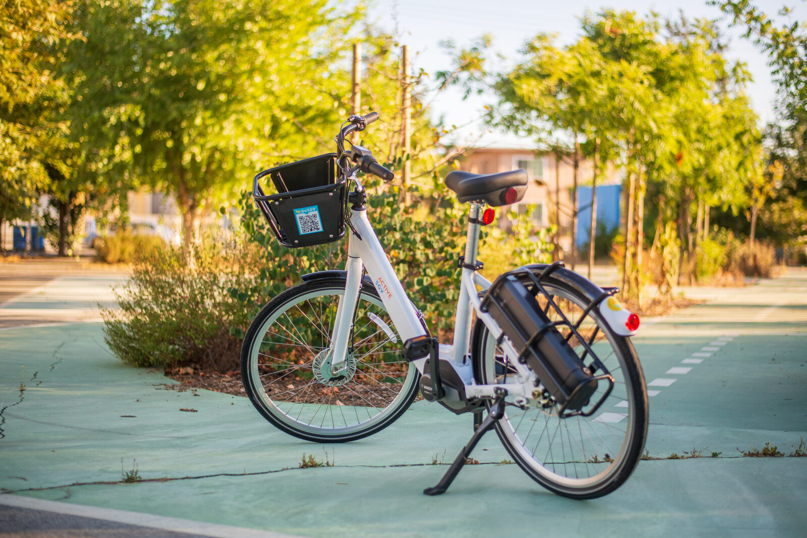 White Classic Commuter e-bike with front basket and rear battery, parked on a green bike path.
