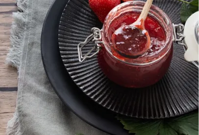A jar of homemade strawberry jam with a wooden spoon on a black plate.