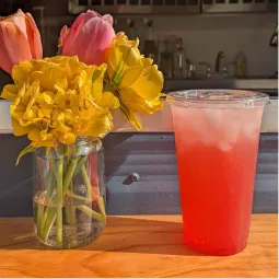 A vibrant summer drink next to a vase of colorful flowers.
