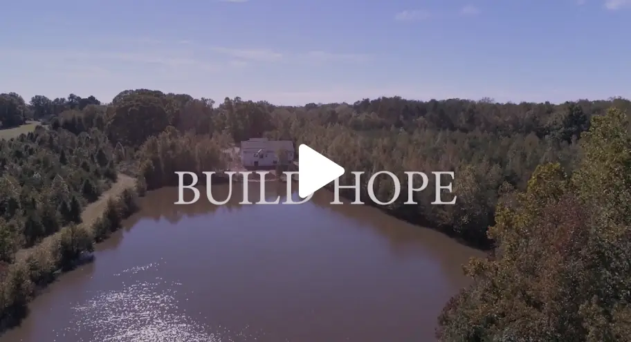 A tranquil lake surrounded by trees with the words 'Build Hope' overlaying the scene.