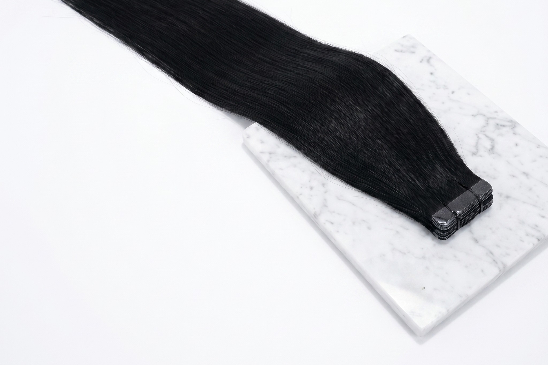 Black long hair extension piece resting on a white square foam block against a white background.