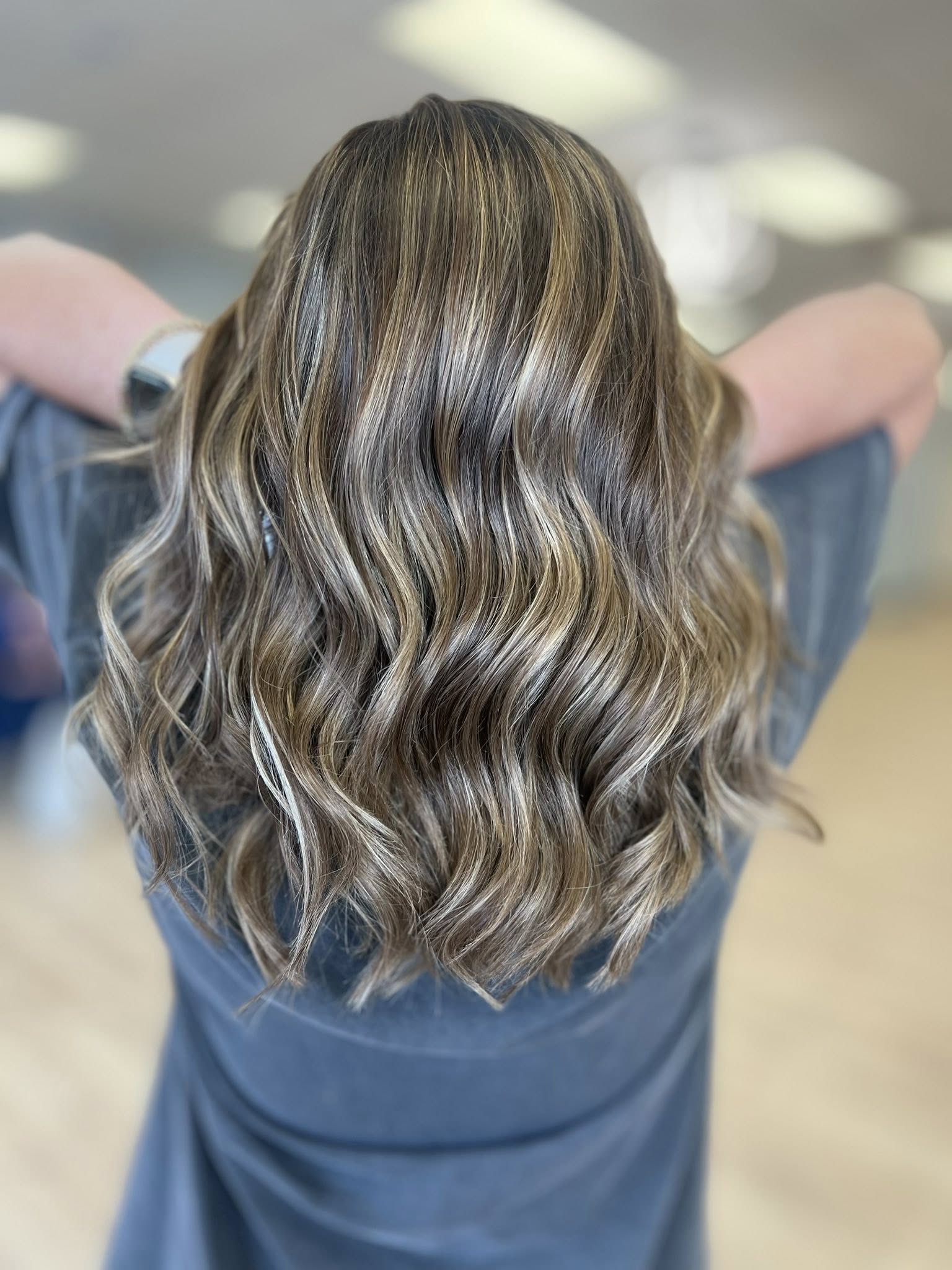 Back view of person with long, wavy hair with blonde highlights wearing a gray shirt.