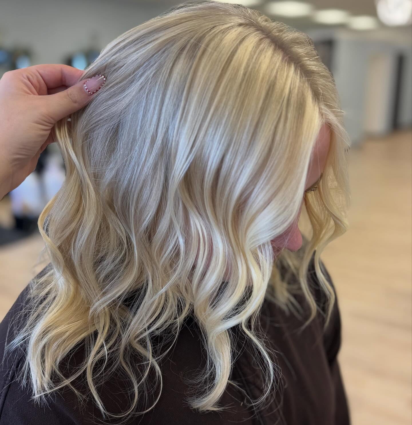 Close-up of a person with shoulder-length wavy blonde hair being held to show its texture.