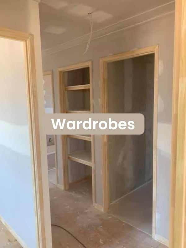 Interior view of an unfinished room with wooden-framed open wardrobes and shelves in a construction setting.