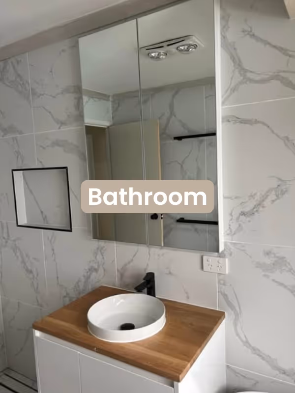 Modern bathroom with marble-patterned tiles, a wooden vanity with white round basin, black faucet, and mirrored cabinet.