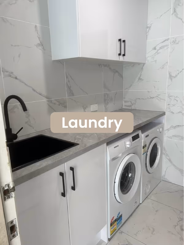 Modern laundry room with white cabinets, gray countertop, black sink and faucet, and front-loading washer and dryer.