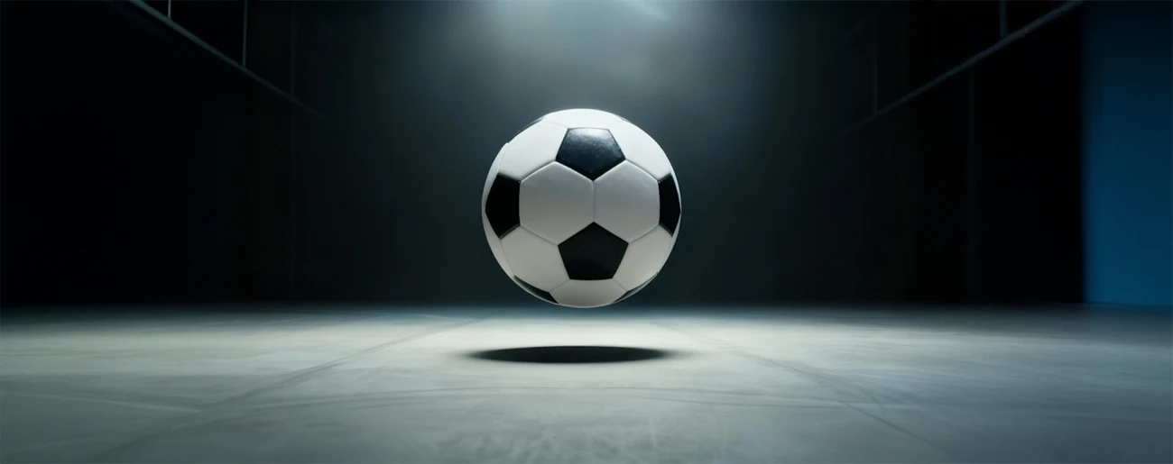 Black and white soccer ball suspended in midair casting a shadow on the floor in a dimly lit room.