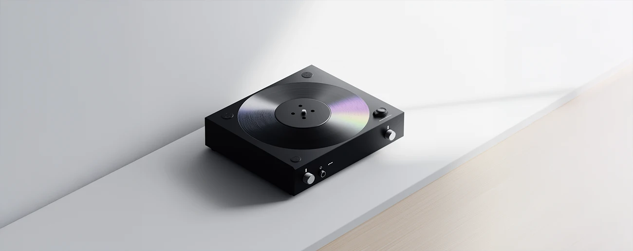 Modern black turntable with a vinyl record on a white surface against a light gray wall.