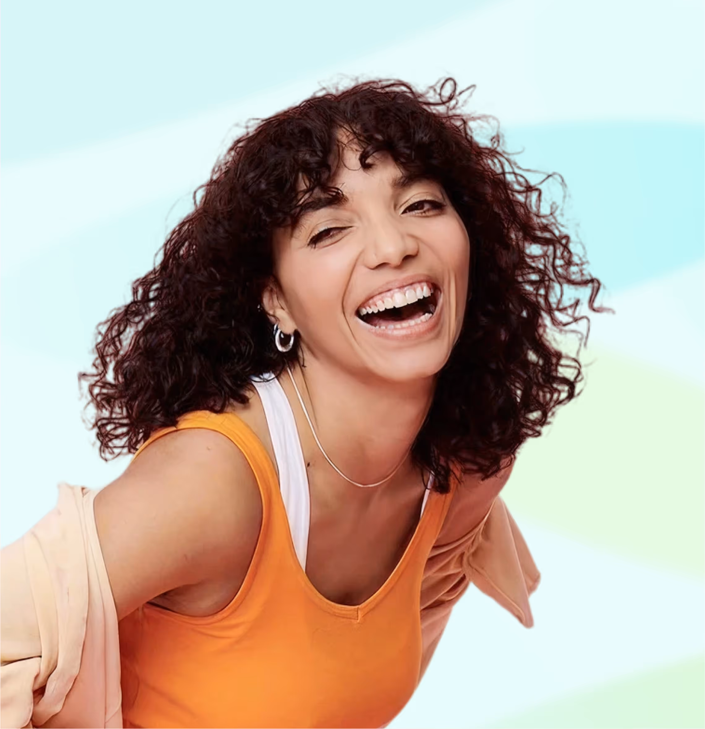 Smiling woman with curly hair wearing orange tank top and white inner shirt against pastel background.
