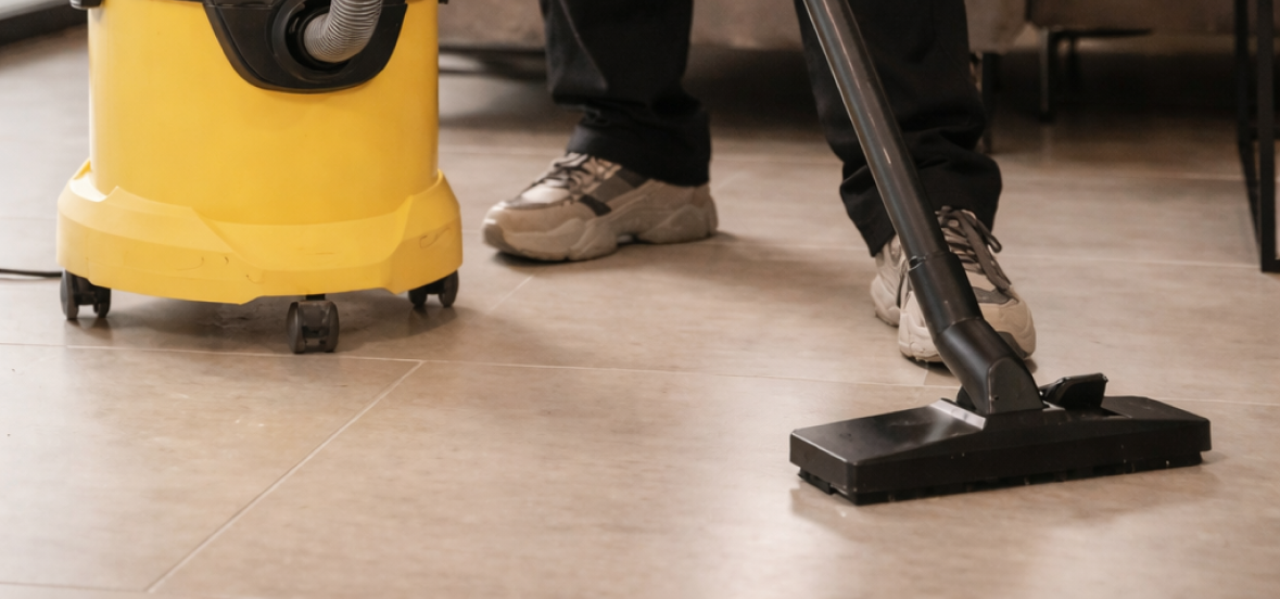 Person vacuuming a tiled floor with a yellow canister vacuum cleaner.