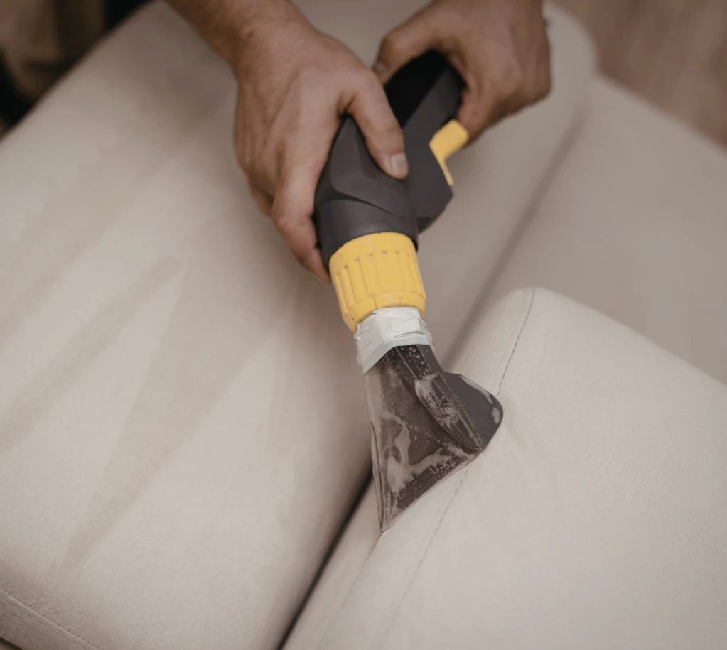 Handheld carpet or upholstery cleaner extracting dirt and foam from a light beige couch cushion.