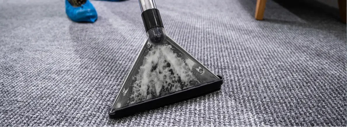 Cleaning a gray carpet with a carpet cleaning machine spraying foam.