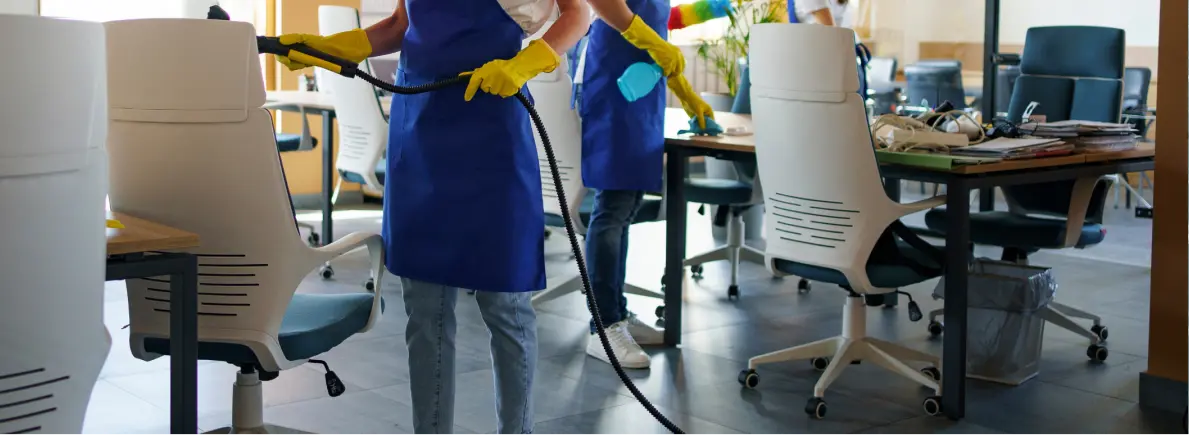 Two people in blue aprons and yellow gloves cleaning an office space with white chairs and desks.