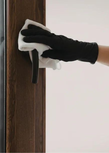 Hand wearing a black glove cleaning a dark wood door handle with a white cloth.