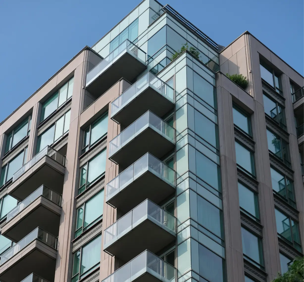 Modern apartment building with multiple glass balconies and large windows under a clear blue sky.