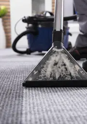 Carpet being cleaned with a professional steam cleaner releasing steam and dirt.