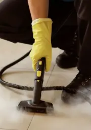 Person wearing yellow gloves using a steam cleaner on a surface emitting steam.