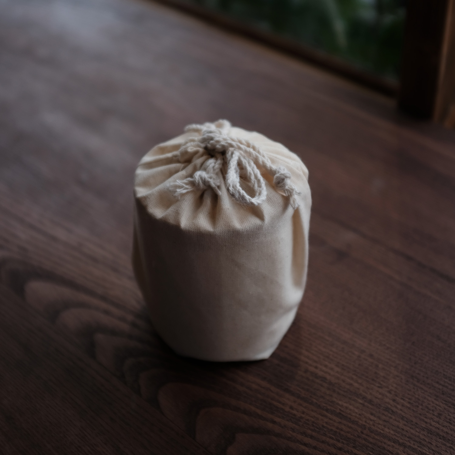 Small beige drawstring pouch placed on a wooden surface.
