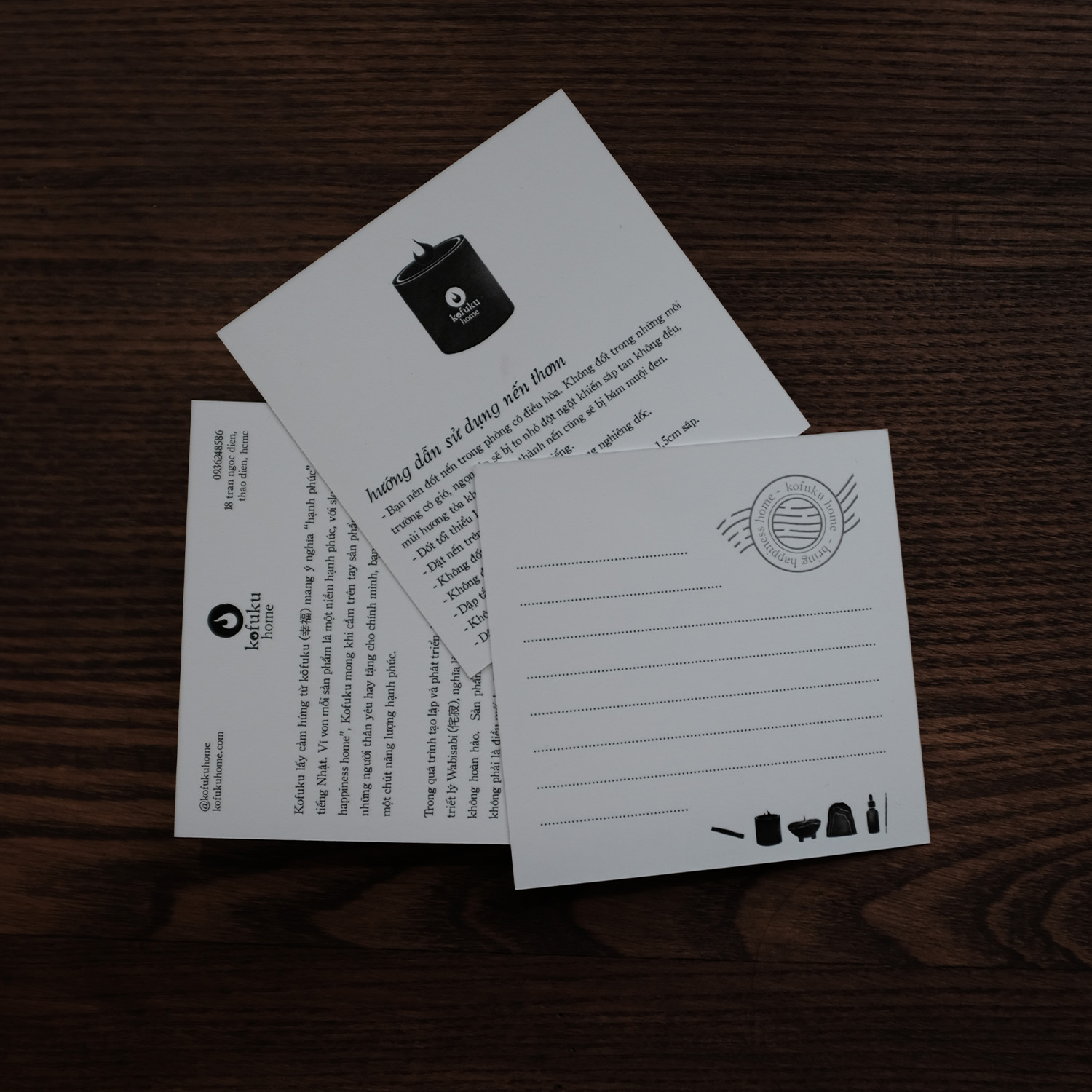 Two postcards on a dark wooden surface, one showing usage instructions for a candle in Vietnamese and the other blank with a stamp and dotted lines for writing.