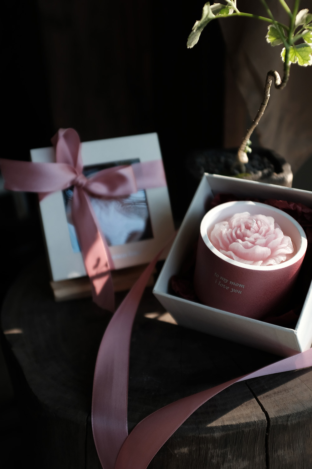 Pink flower-shaped candle in a maroon holder with 'to my mom i love you' text, in an open white gift box with pink ribbon nearby.