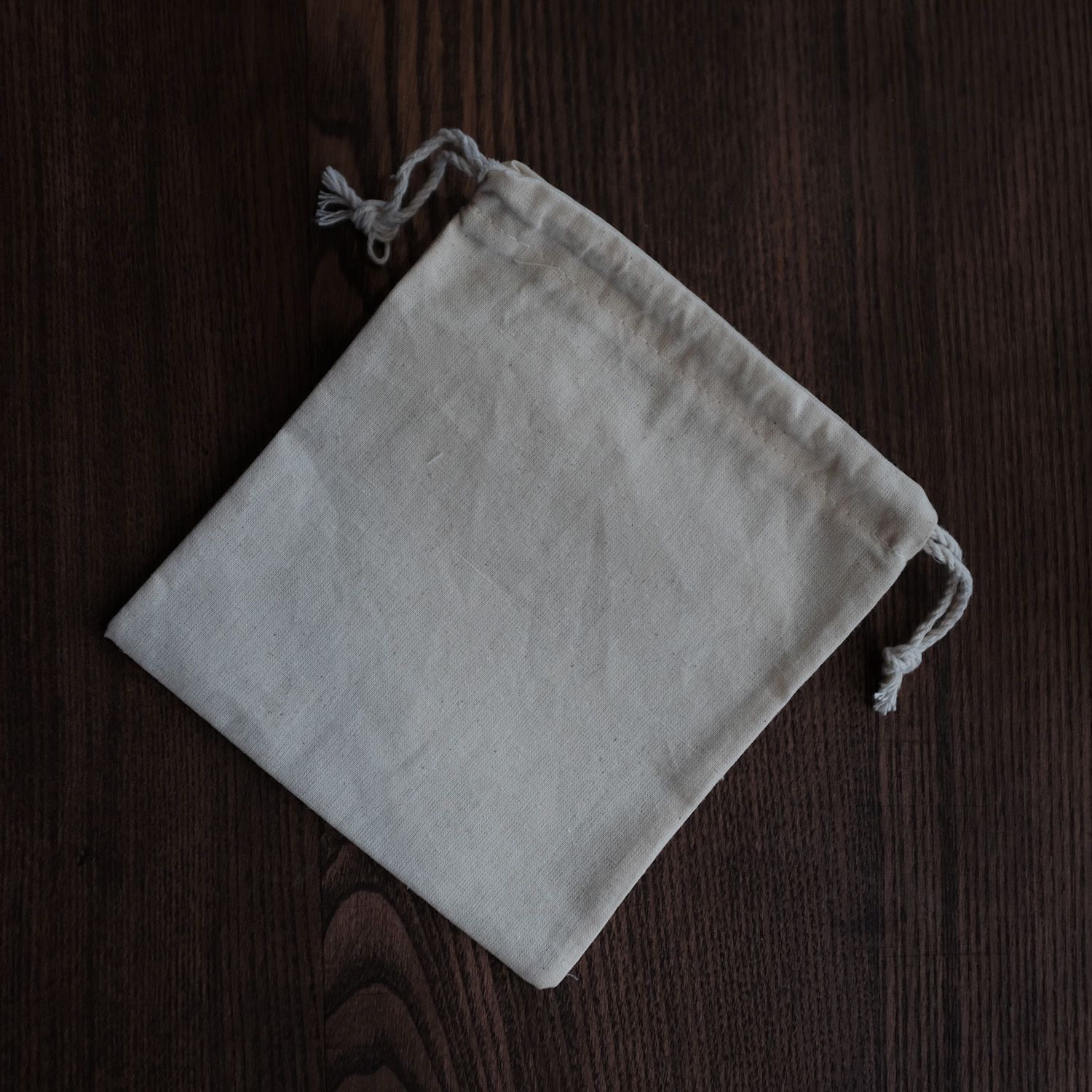 White drawstring cloth bag on a dark wooden surface.