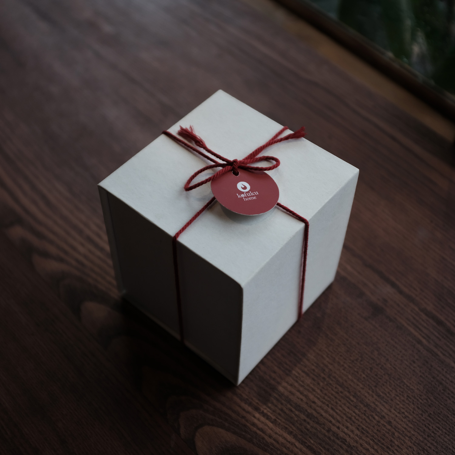 A white gift box tied with red string and a round red tag reading 'koifuku home' on a wooden surface.
