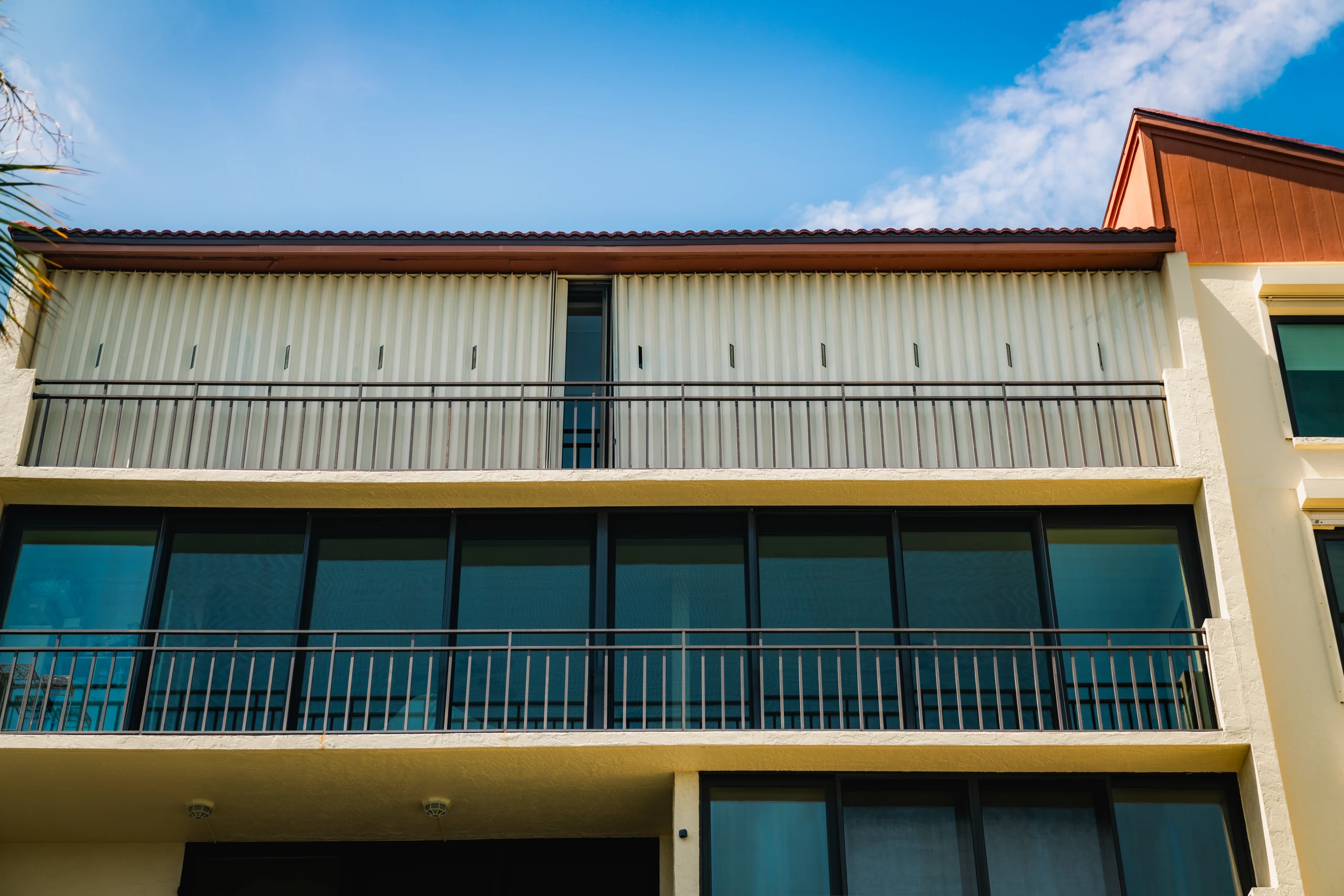 Condo building with roll-down hurricane shutters closed on the upper balcony