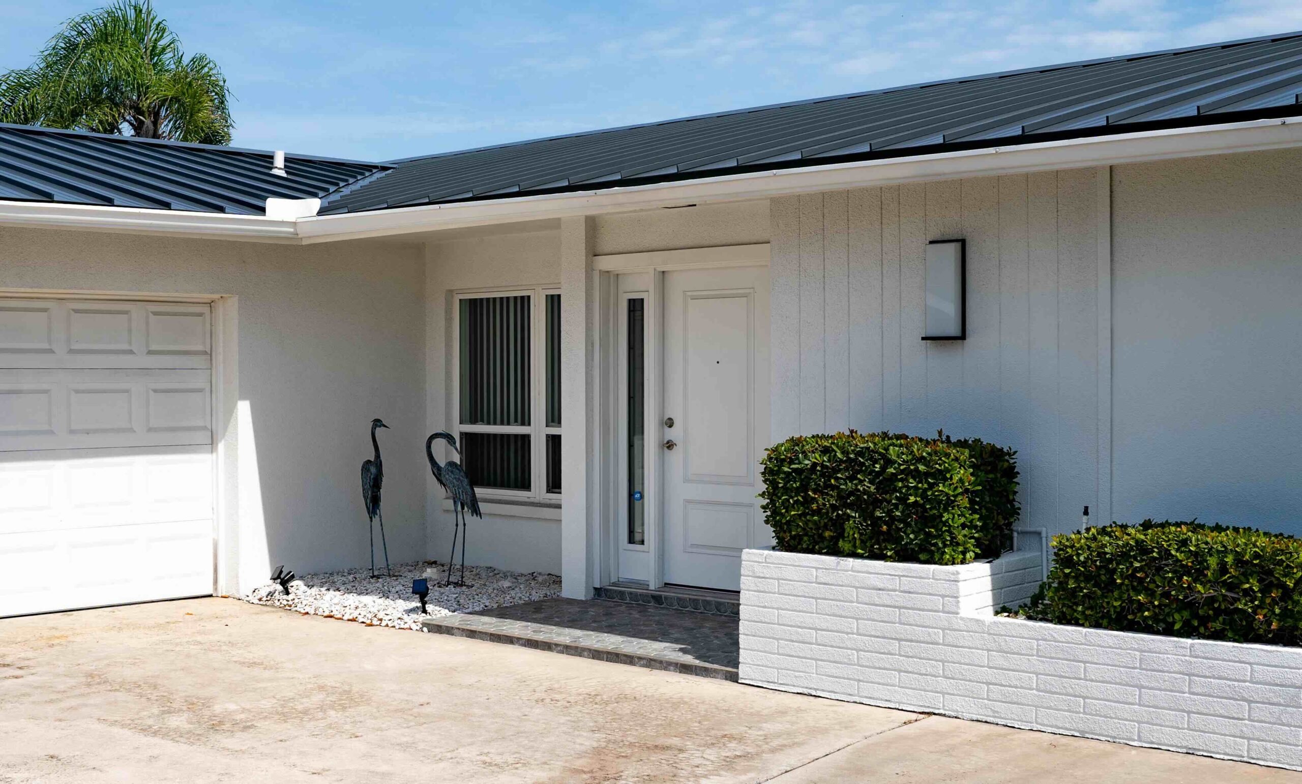 Photo of one-story white house with a new black roof. A palm tree is visible in the background.