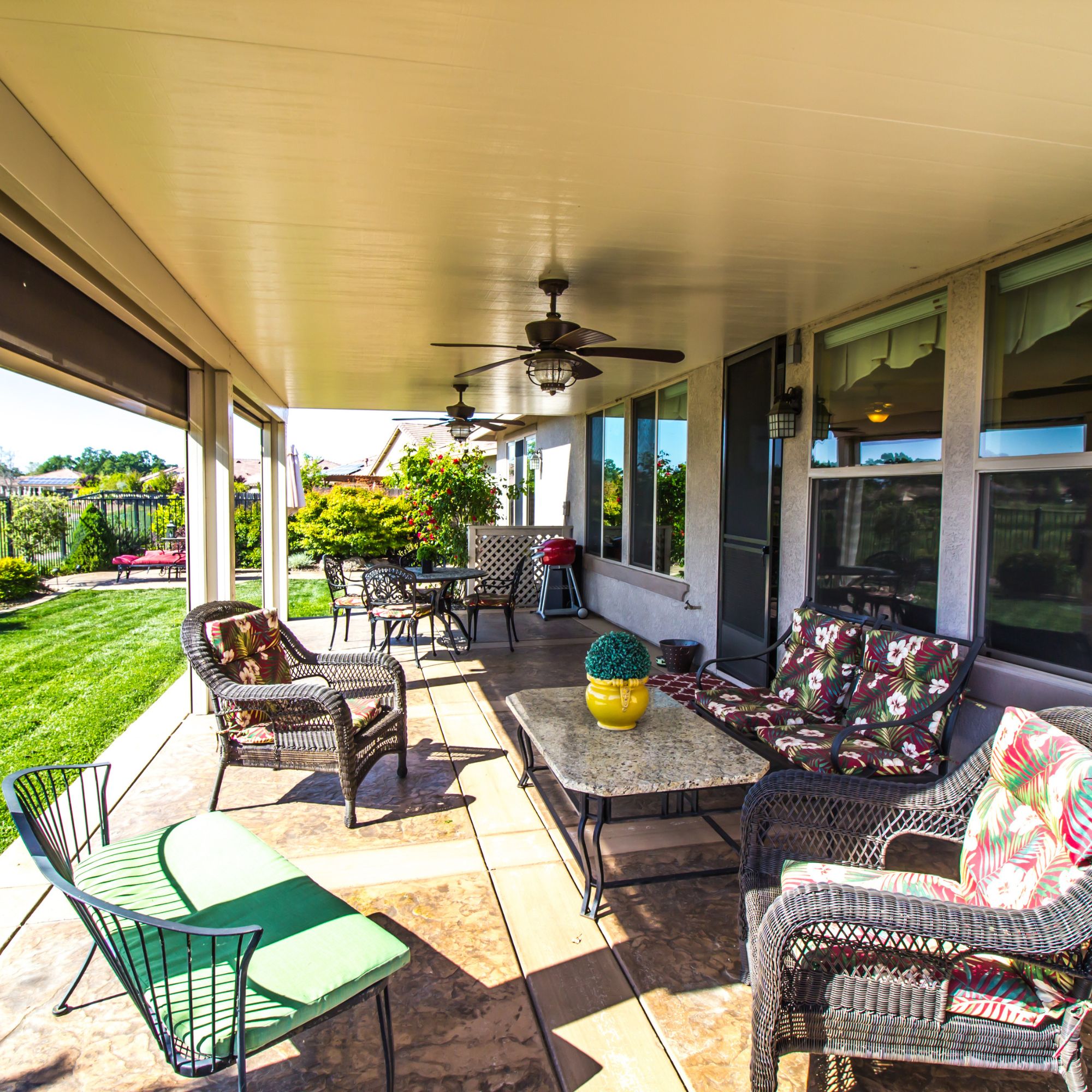 Covered patio with a flat aluminum roof, ceiling fans and wicker seating