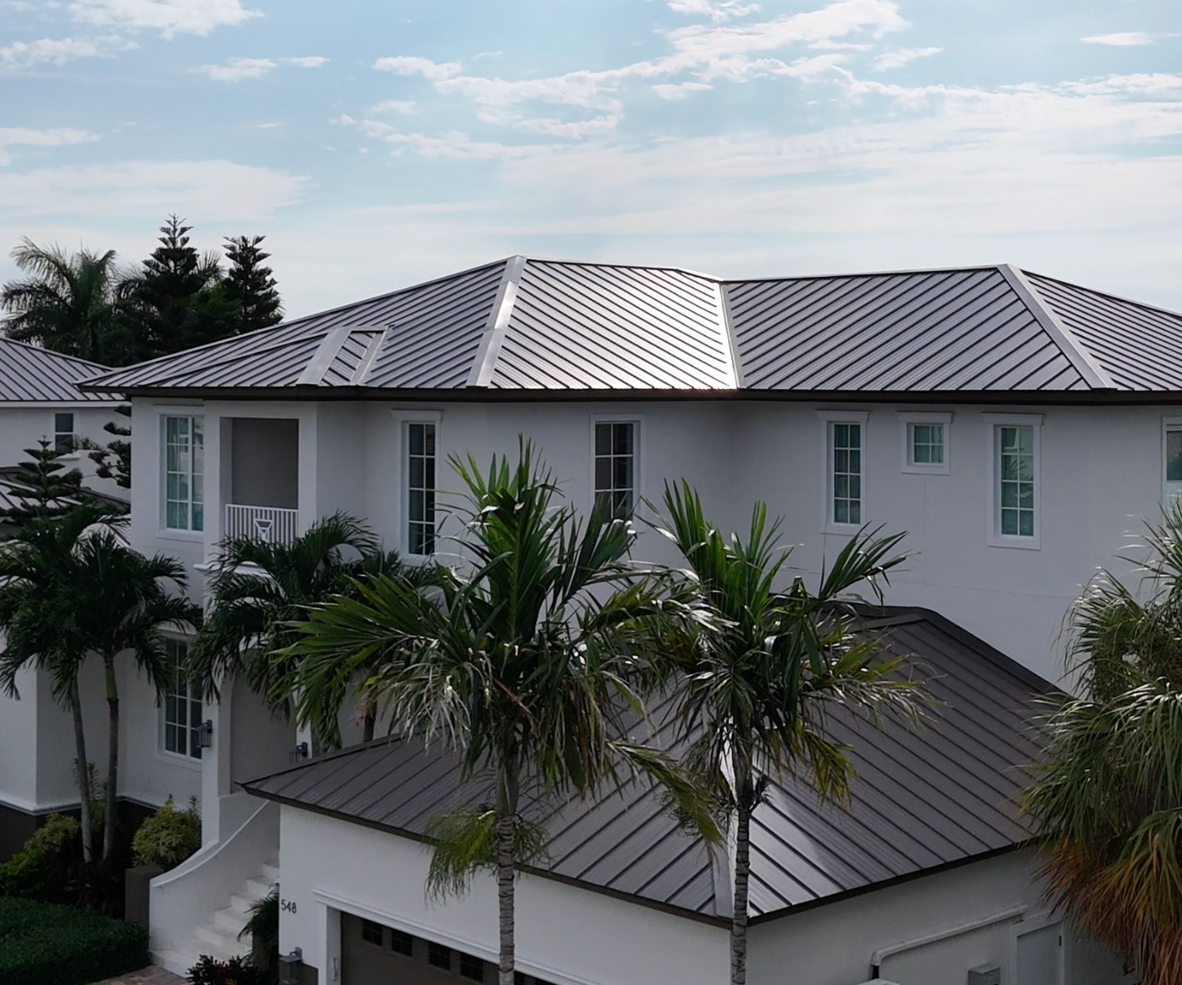 Standing seam metal roof on a coastal home framed by palm trees