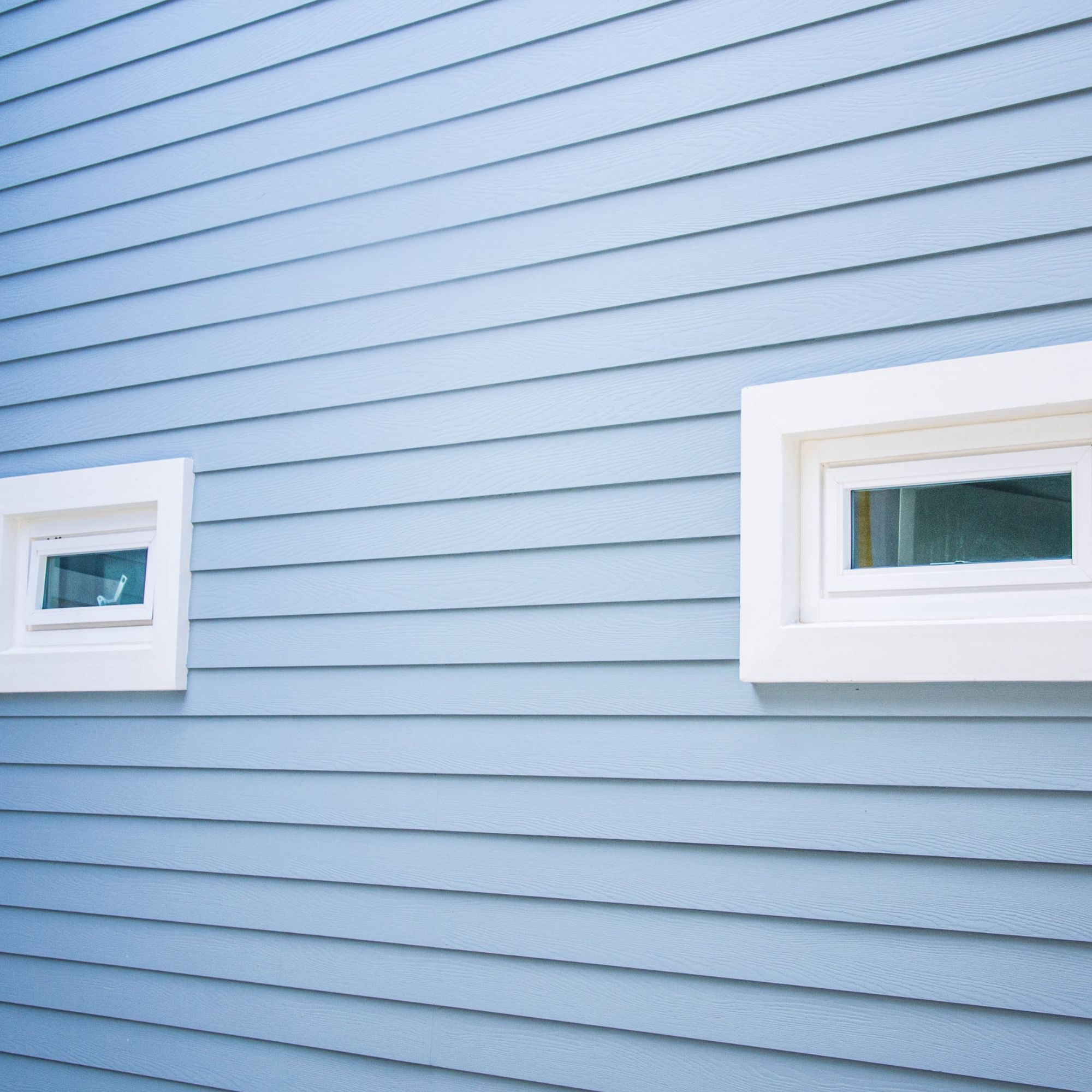 Close-up of light blue fiber cement lap siding with white window trim