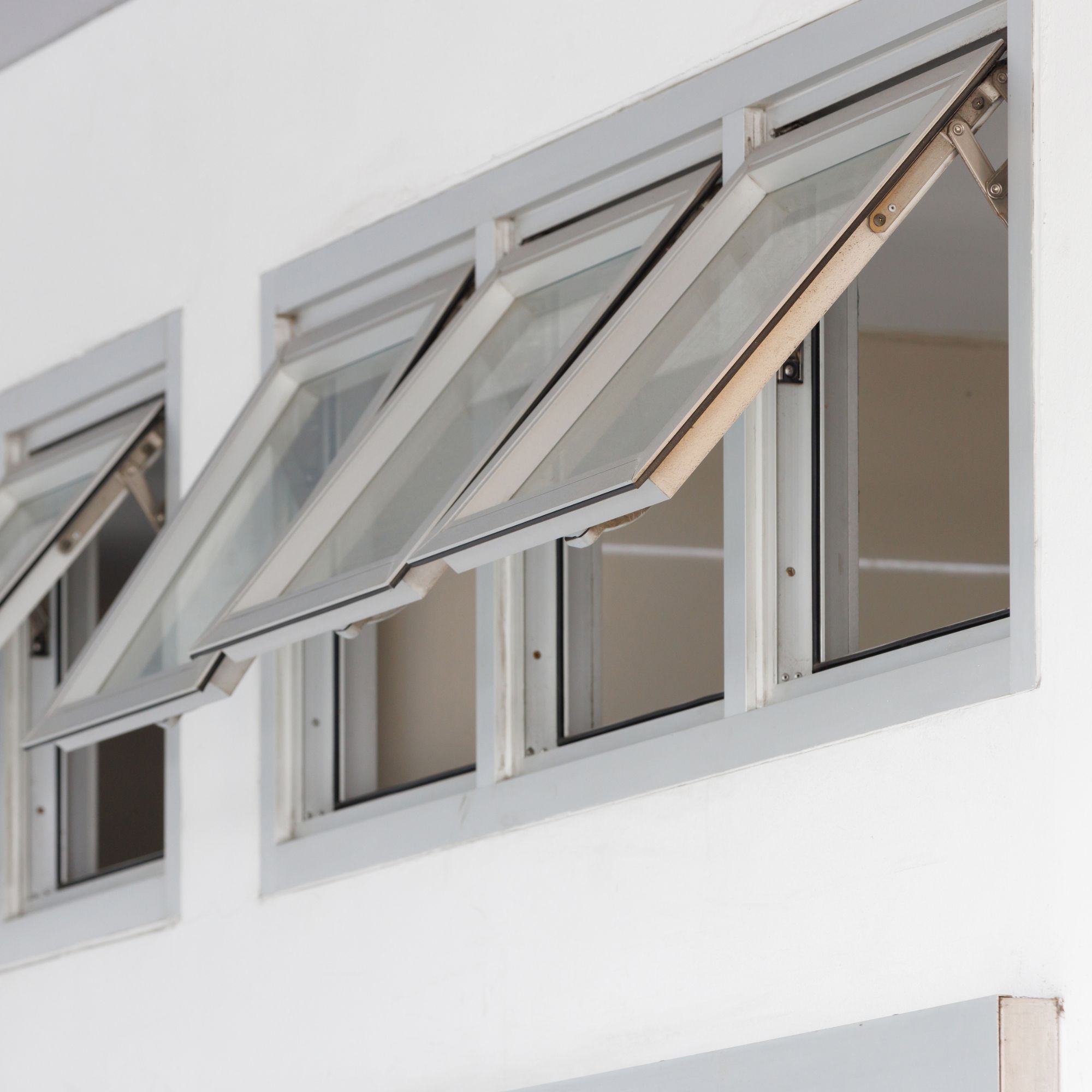 Row of awning windows cranked open on a white stucco wall