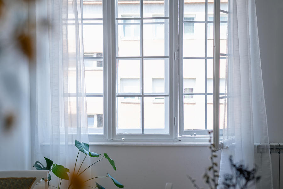 White casement windows open inward beside sheer curtains
