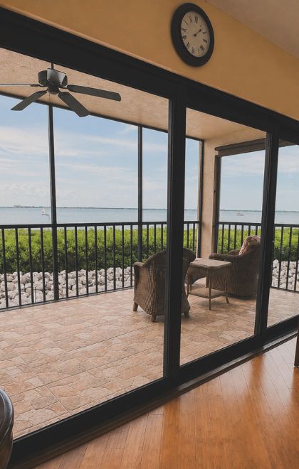 Screened lanai enclosure with wicker seating overlooking the bay