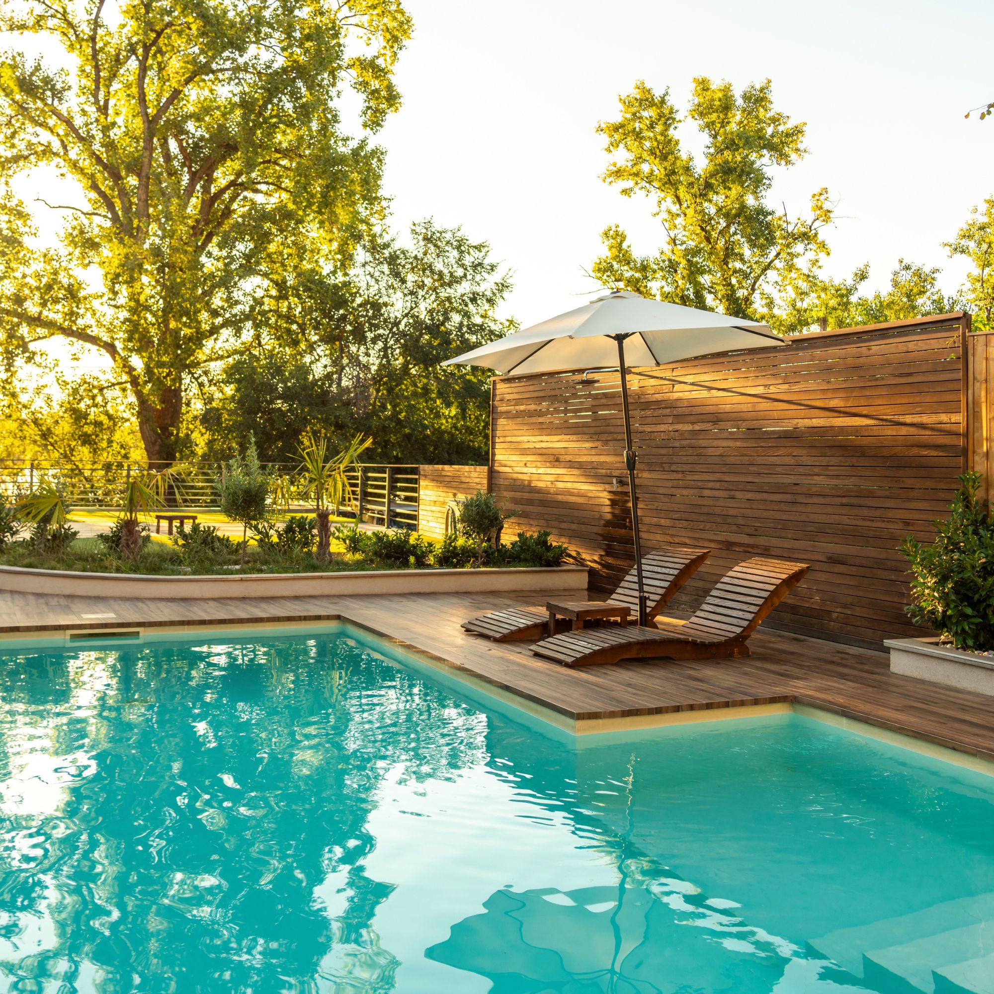 Pool deck with wood loungers, an umbrella and a privacy fence
